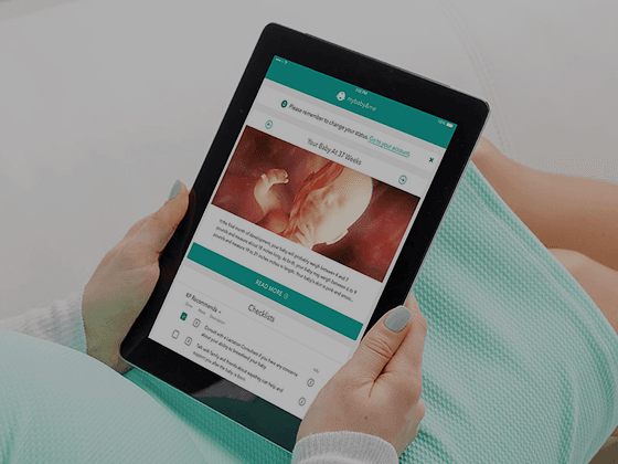 Person seated, holding a tablet that displays a medical app with a fetal ultrasound image and teal interface.