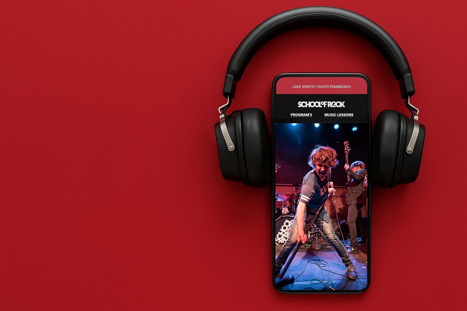 Vertical smartphone surrounded by large black over-ear headphones on a red background; screen shows a live rock band performance with a guitarist center stage.