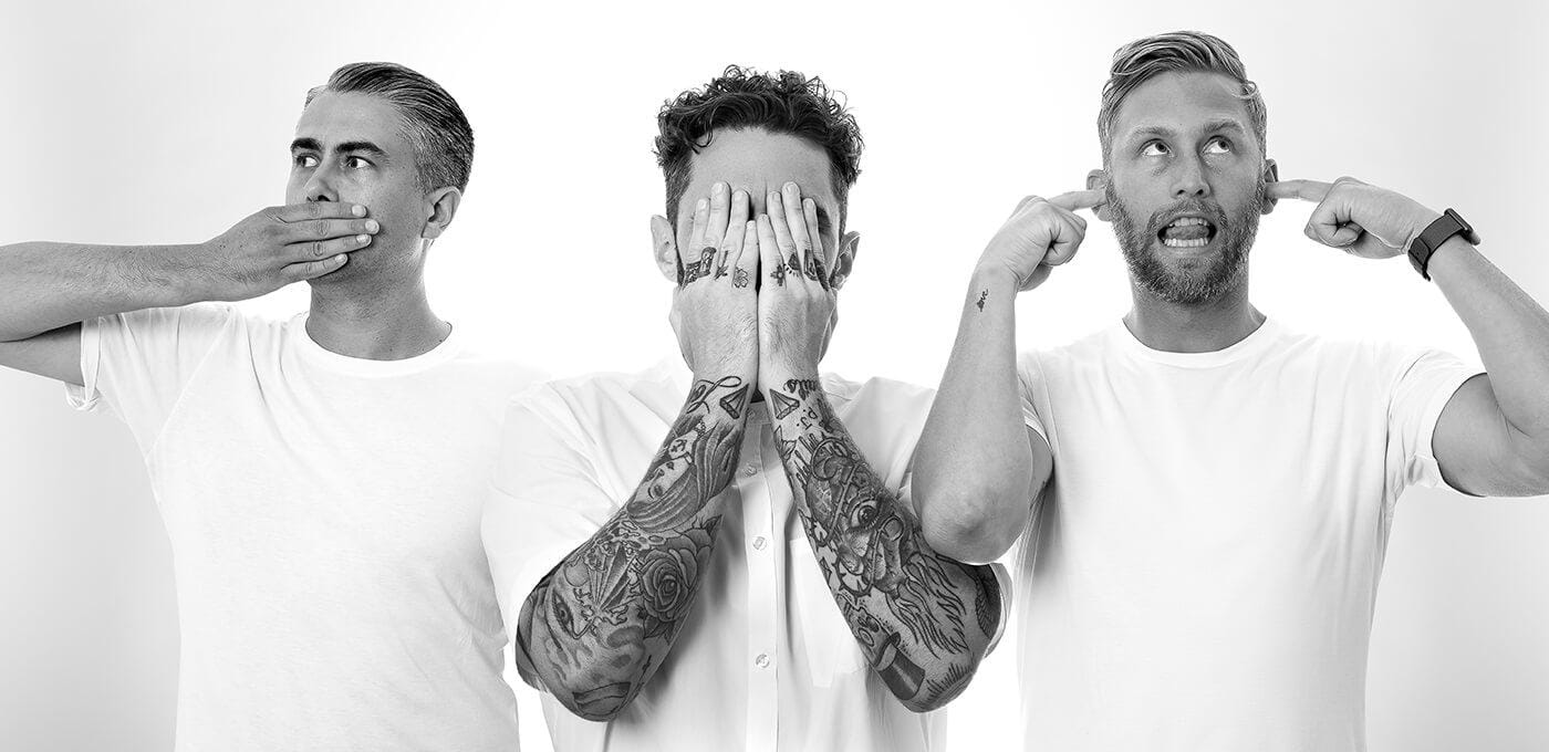 Three individuals in white T‑shirts stand side by side: left covers the mouth, center shields the face with tattooed arms, right plugs the ears.