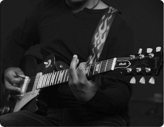 Close-up of a musician playing an electric guitar in grayscale, with hands on the fretboard and strumming, a flame-pattern strap.