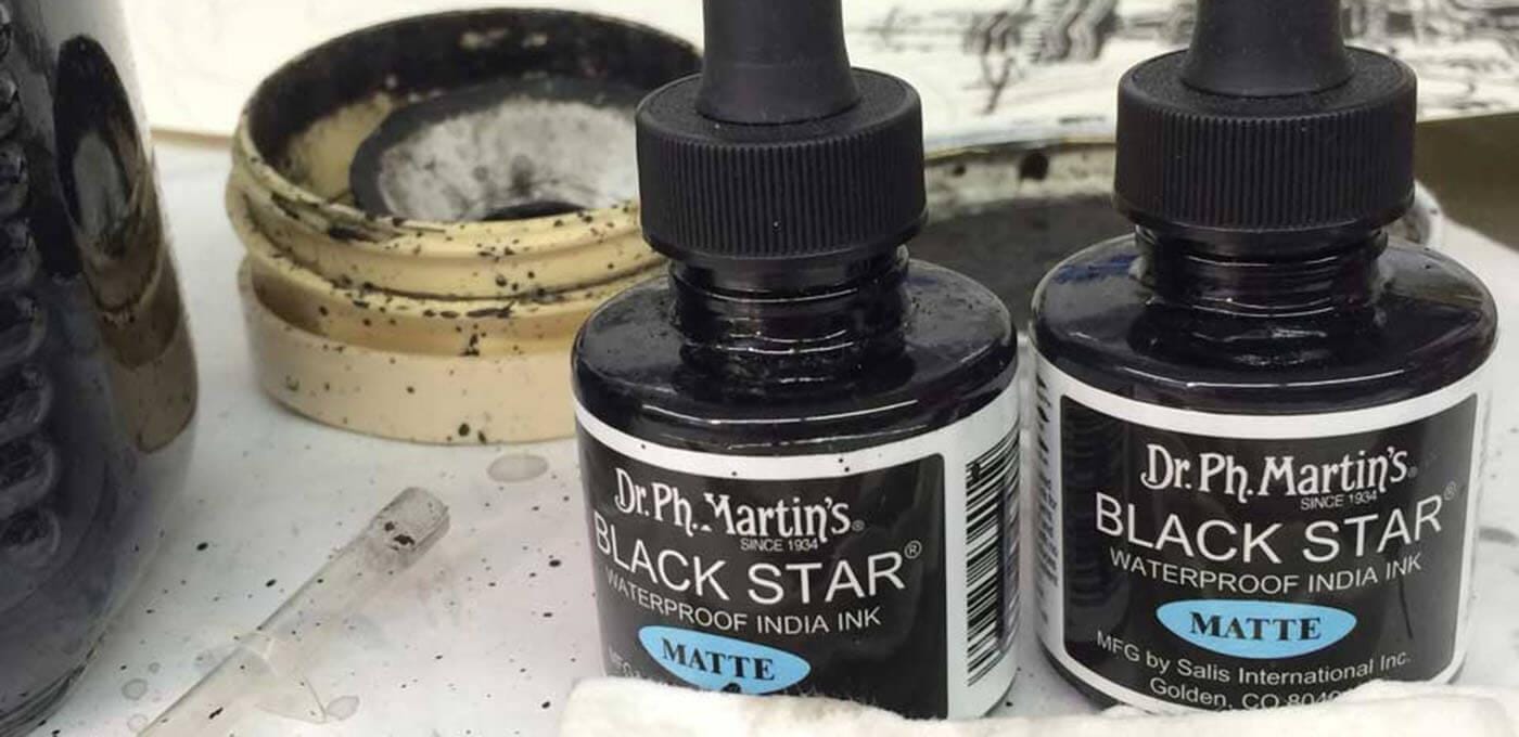 Two bottles of Dr. Ph. Martin's Black Star Matte waterproof India Ink with dropper tops on a stained studio desk, surrounded by ink splatters.