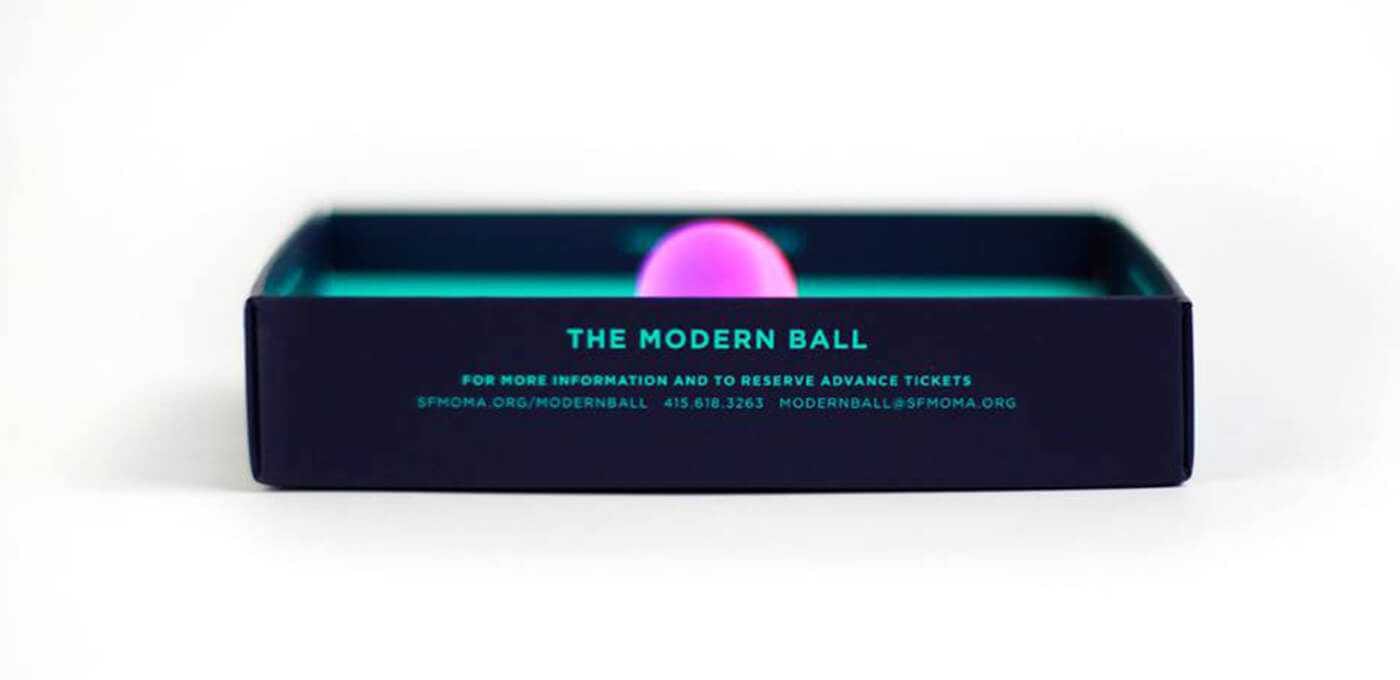 Open navy rectangular box with a teal interior glow; a pink ball sits inside, and the front reads 'THE MODERN BALL' in turquoise text.
