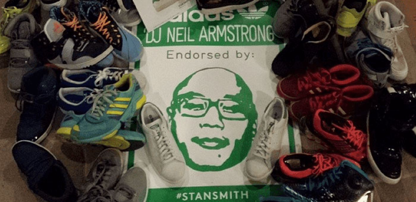 A circle of colorful sneakers surrounds a white poster with a green stylized face and the words “Endorsed by” and “#STANSMITH.”