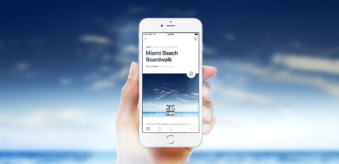 Hand holds a white iPhone displaying a page titled 'Miami Beach Boardwalk' with a beach photo, against a blue sky and ocean backdrop.