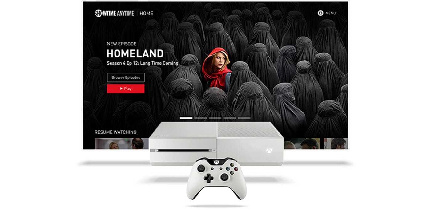 White Xbox One S console and controller in front of a TV screen showing Homeland artwork with a red-hooded person among dark hooded figures.