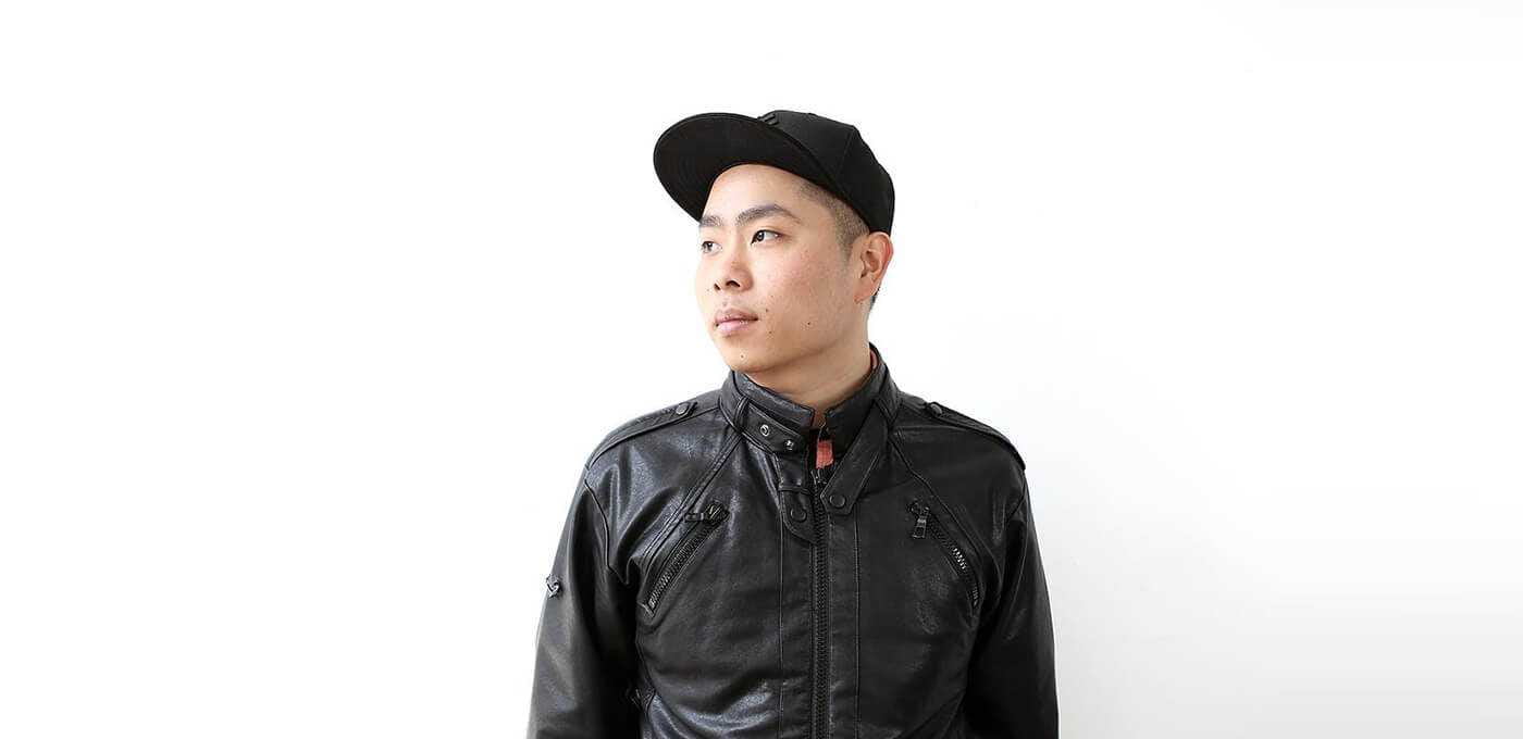 Person wearing a black leather jacket and black cap, looking to the left, against a plain white background.