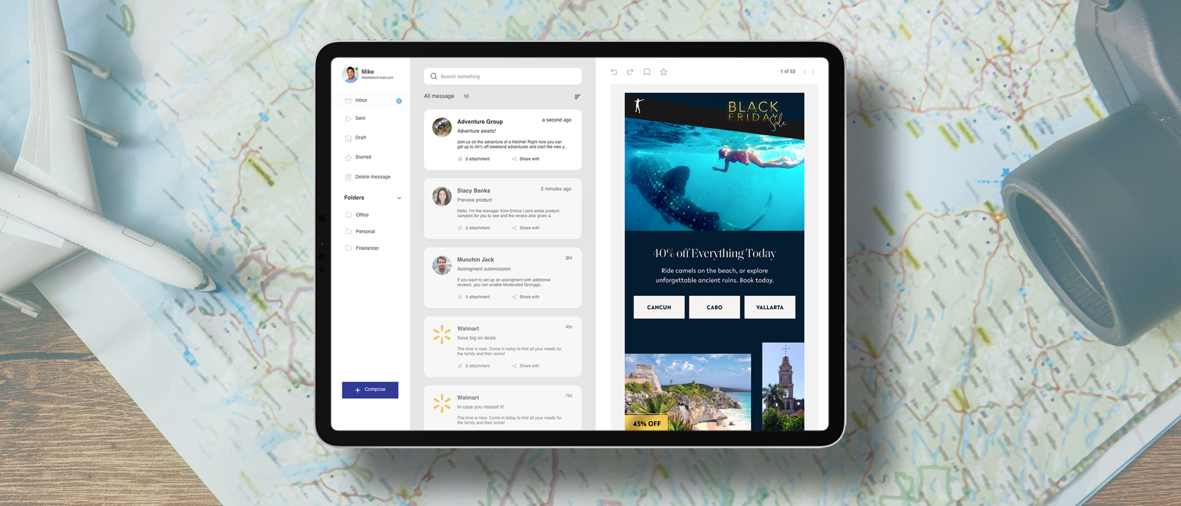 Tablet on a map-covered desk showing a split screen: left an inbox messages panel, right an underwater Black Friday ad; a toy airplane and mug nearby.