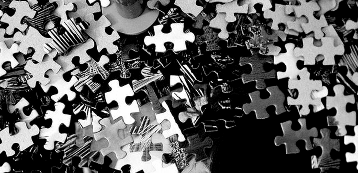 Monochrome collage of interlocking jigsaw pieces scattered across a high-contrast mix of light and dark shapes.