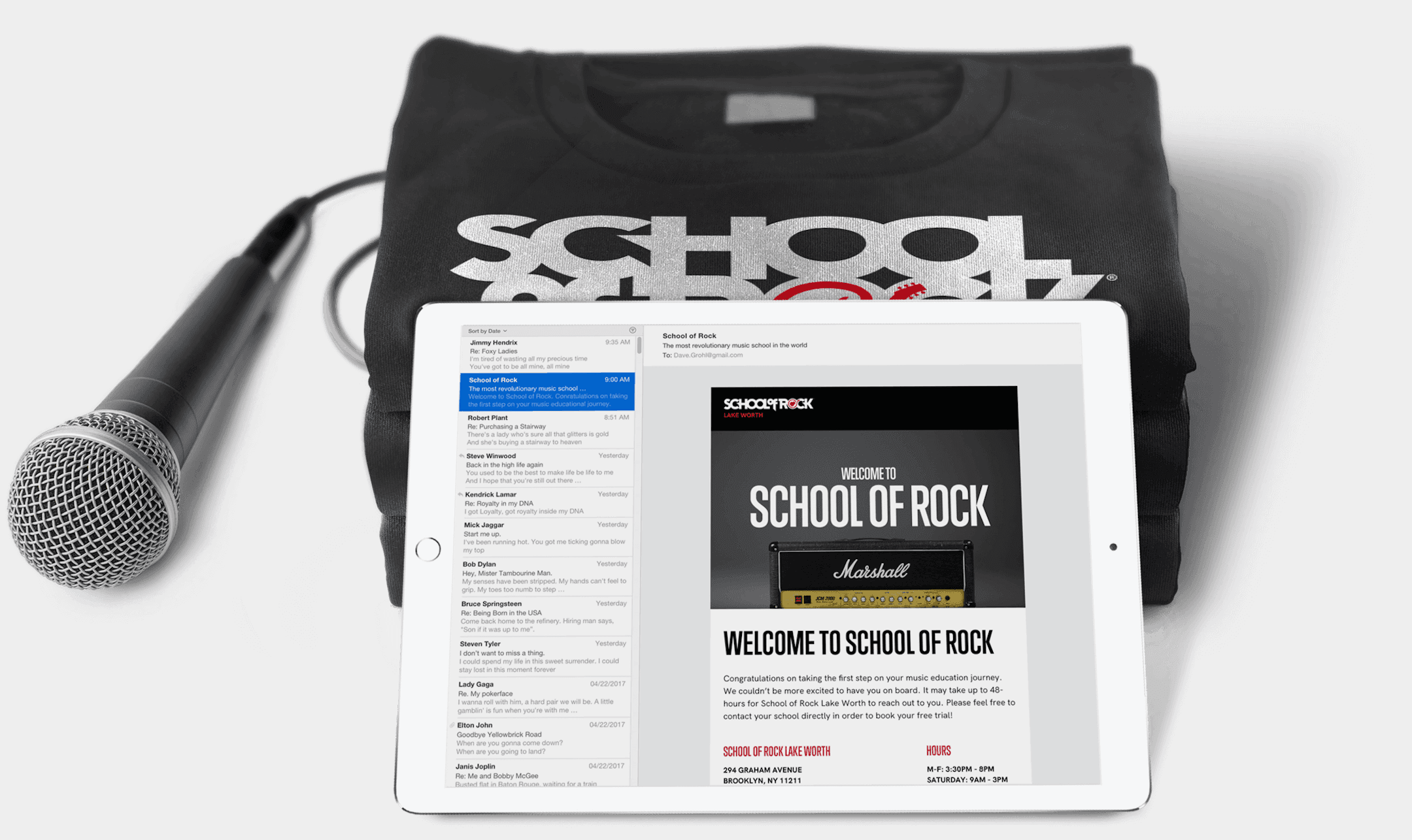 Black t-shirt with bold white 'SCHOOL' text, over a tablet showing a 'Welcome to School of Rock' flyer and Marshall amp image, with microphone nearby.