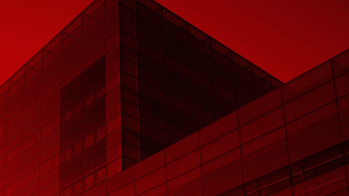 Red-tinted view of a modern glass building with grid-like windows and sharp diagonal edges.
